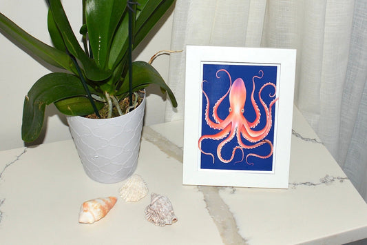 Framed artwork of an octopus on a marble surface with a plant and shells.