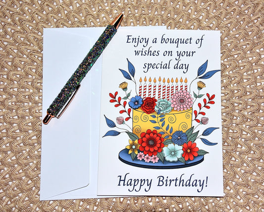 Birthday card with hand illustrated colorful cake and surrounding flowers and candles with white envelope, dark green glitter pen on textured surface