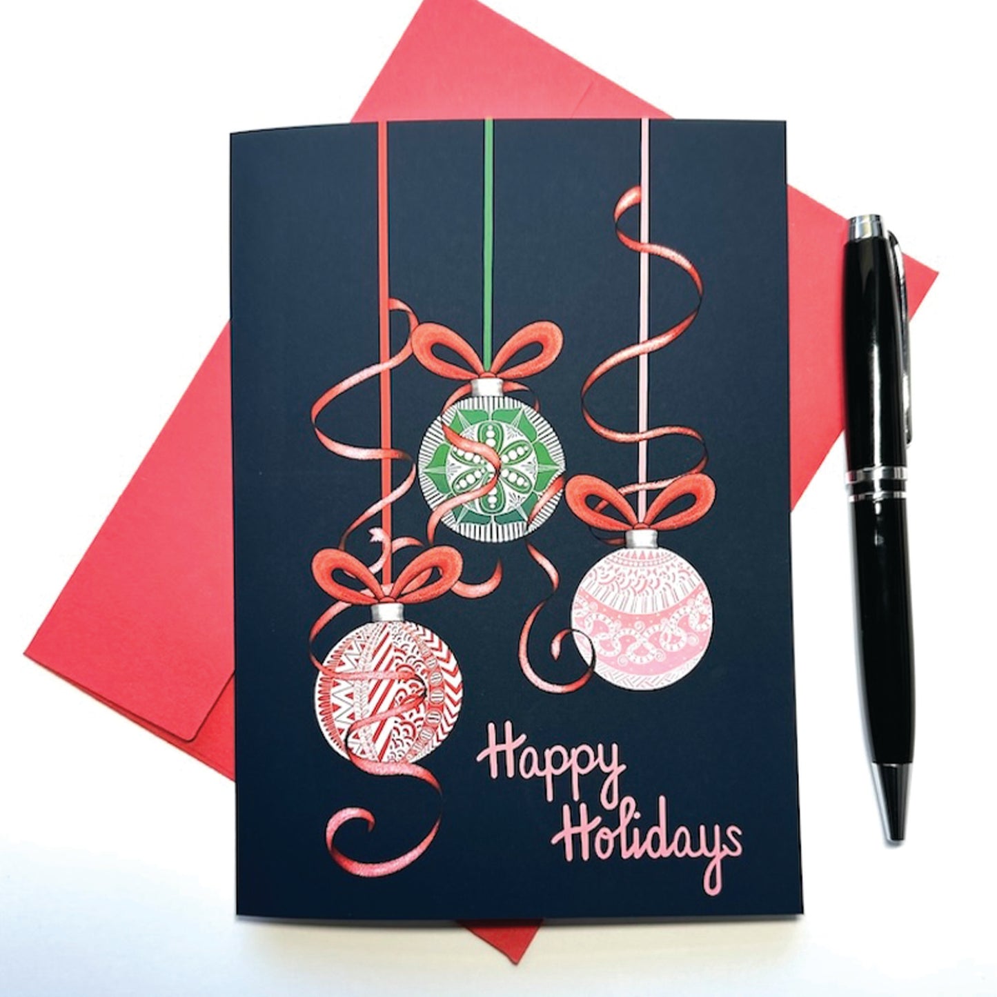 Holiday card with hanging ornaments adorned with red ribbon and 'Happy Holidays' text, red envelope, and pen on white background