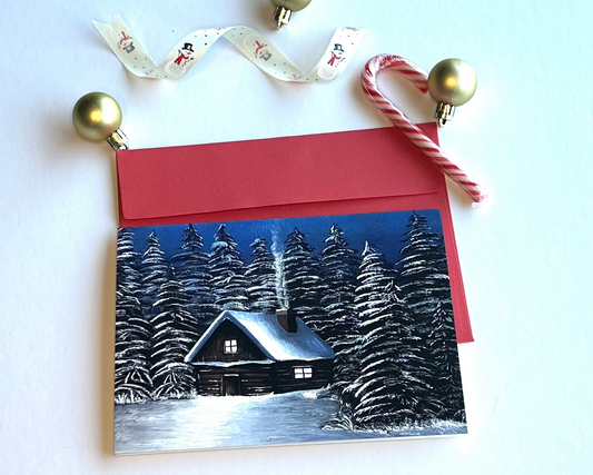 Card with painting of a winter scene of a cabin in the woods, decorated with Christmas ornaments on a white background.