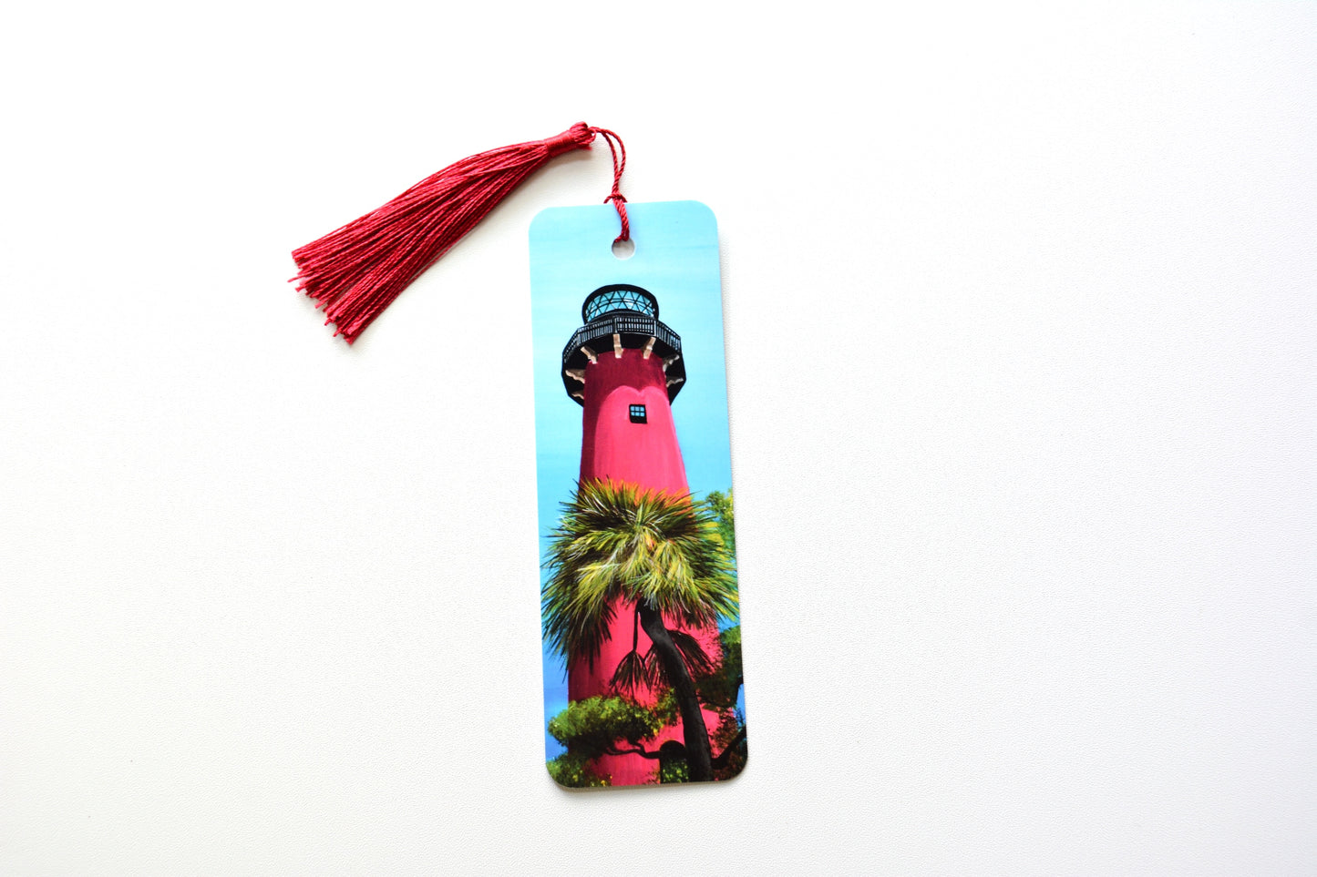 Bookmark with the Jupiter Lighthouse and palm trees design with red tassel placed on a white surface