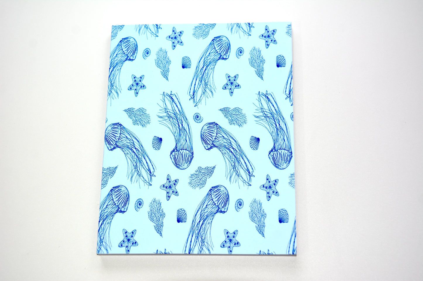 Notebook with a pattern featuring navy blue jellyfish, starfish, sea kelp, and starfish pattern on a light blue background