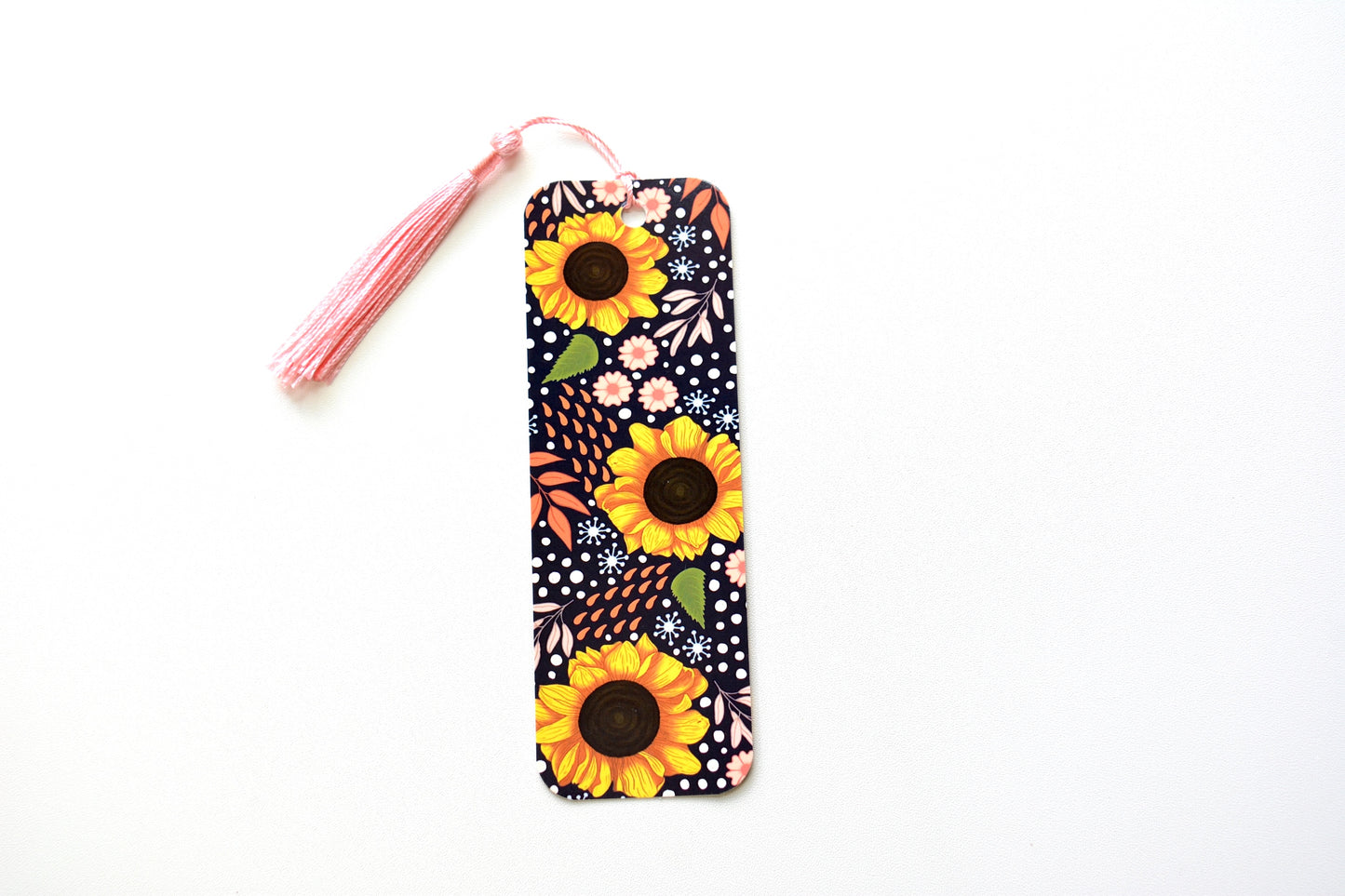 sunflower pattern bookmark with pink tassel placed on a white surface 