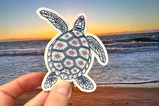 Decorative turtle vinyl sticker held over a beach with ocean waves and sunset.